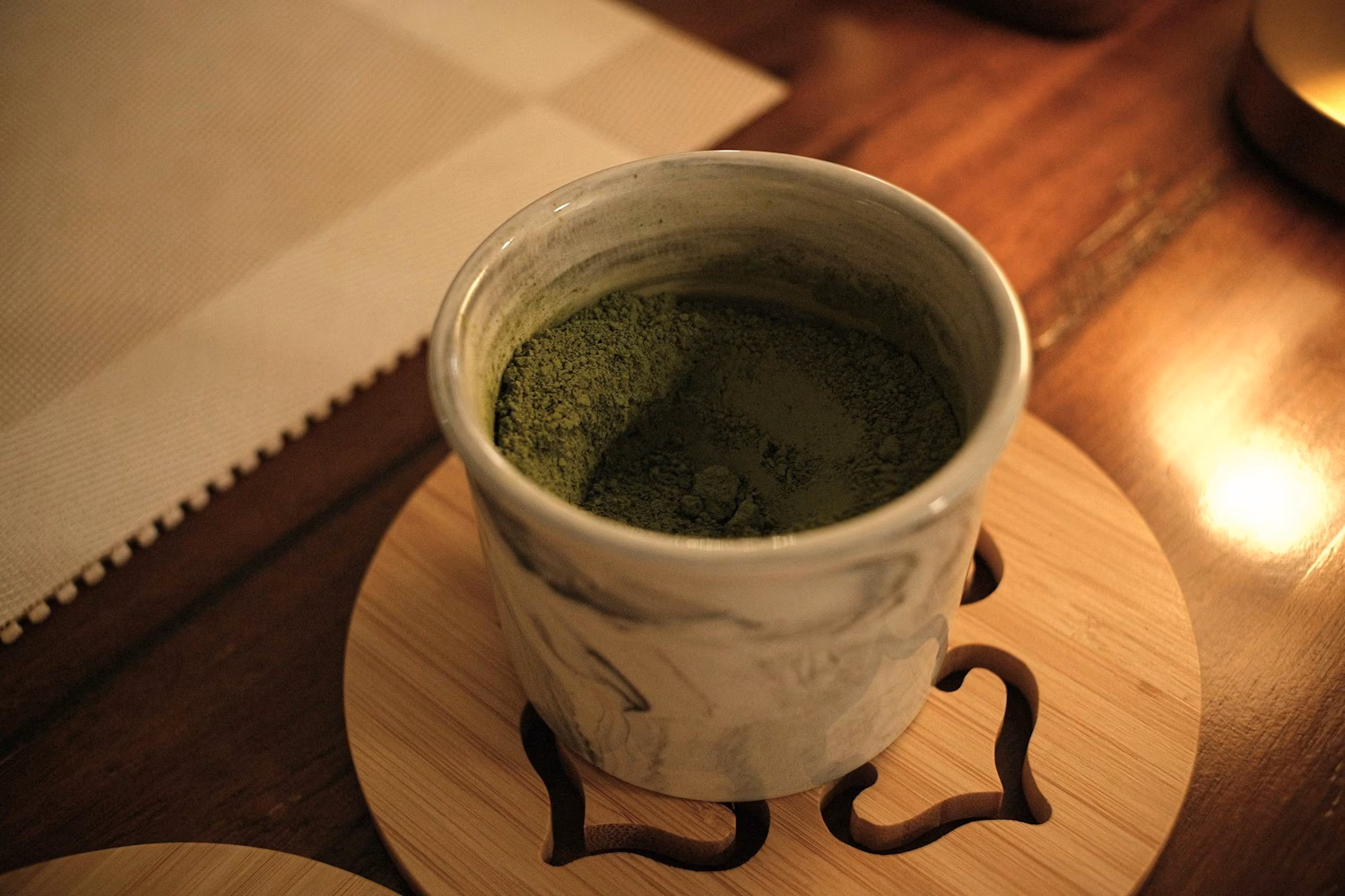 Matcha powder in a ceramic cup on a wooden coaster